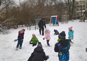 Zdjęcie przedstawia zabawy dzieci z wolontariuszem na śniegu w ogrodzie przedszkolnym